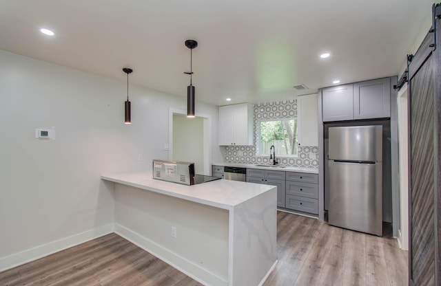 10415 Westray St, Houston, TX 77043 - kitchen featuring appliances with stainless steel finishes, a barn door, light wood-type flooring, decorative backsplash, and a peninsula