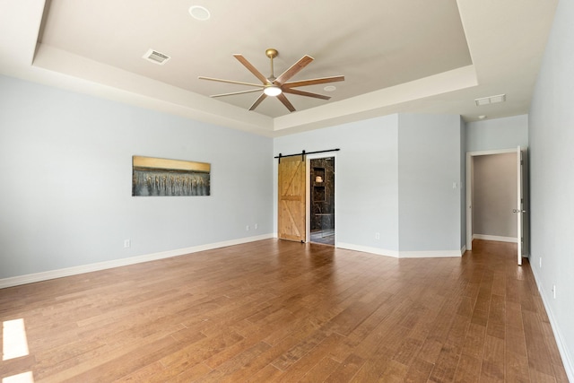 4946 Westchester Dr, Fulshear, TX 77441 - empty room with a tray ceiling, a barn door, ceiling fan, and wood finished floors
