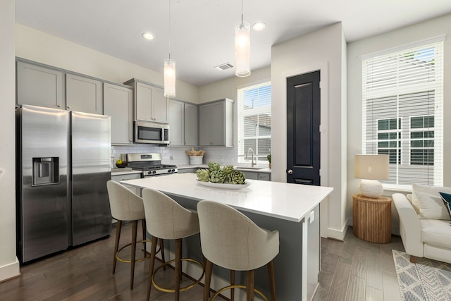 6033 Cypress St, Houston, TX 77074 - kitchen featuring stainless steel appliances, gray cabinetry, backsplash, dark wood-type flooring, and a kitchen breakfast bar