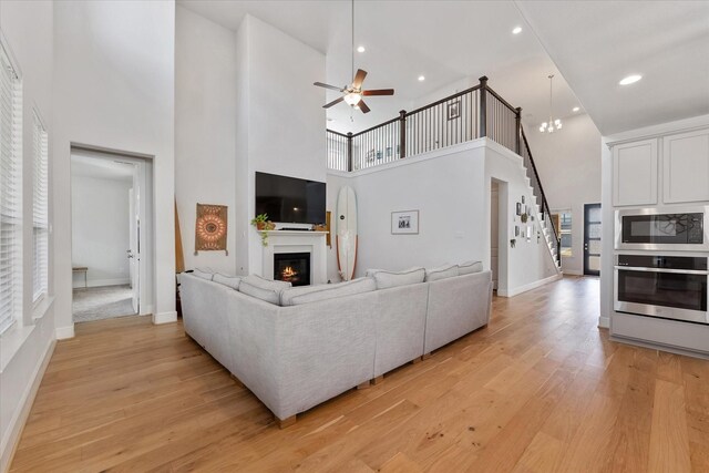 10059 Preserve Way, Conroe, TX 77385 - living room with a towering ceiling, a glass covered fireplace, a ceiling fan, light wood-type flooring, and stairway