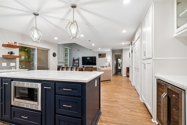 7 Bending Branch Pl, Spring, TX 77381 - kitchen with stainless steel microwave, beverage cooler, white cabinetry, light wood-style floors, and recessed lighting