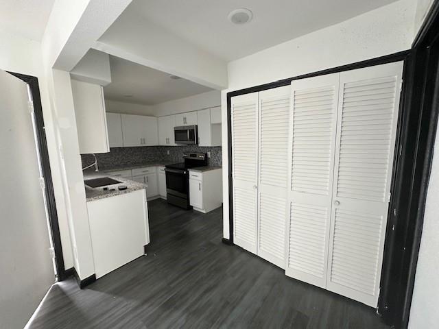 9009 Imogene St Unit E, Houston, TX 77036 - kitchen featuring black electric range, stainless steel microwave, tasteful backsplash, white cabinetry, and dark wood-style floors