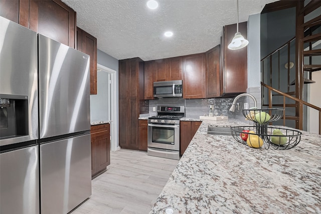9302 Moorfield Ct, Houston, TX 77083 - kitchen featuring appliances with stainless steel finishes, light wood finished floors, backsplash, a textured ceiling, and hanging light fixtures