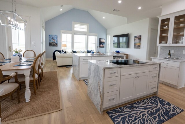 18414 Indian Beach Ct, Galveston, TX 77554 - kitchen with black electric stovetop, a center island, light wood-style flooring, glass insert cabinets, and white cabinetry