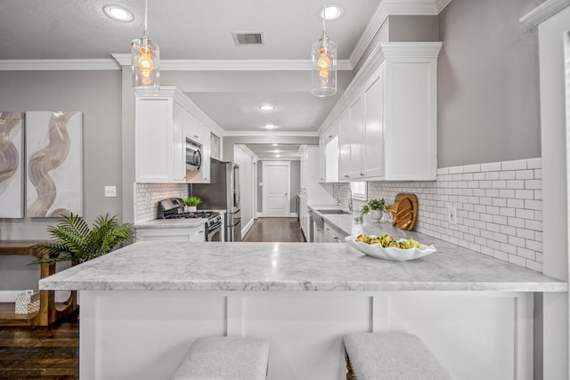 829 E 27th St, Houston, TX 77009 - kitchen with appliances with stainless steel finishes, white cabinets, dark wood finished floors, a peninsula, and ornamental molding