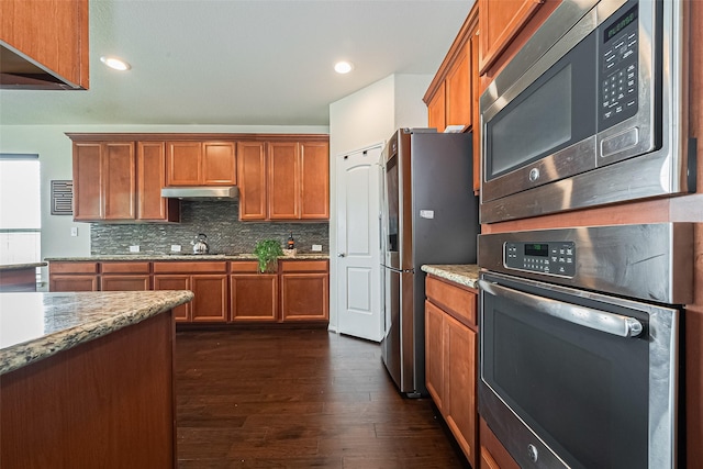 6022 Allendale Ridge Trl, Richmond, TX 77407 - kitchen featuring stainless steel appliances, under cabinet range hood, brown cabinets, dark wood-style floors, and backsplash
