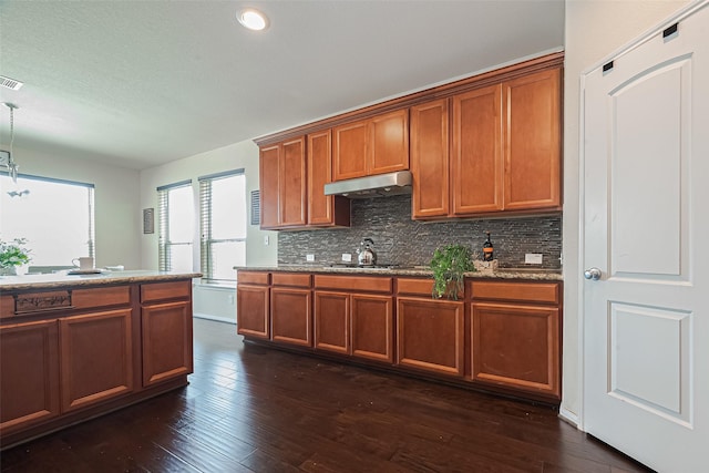 6022 Allendale Ridge Trl, Richmond, TX 77407 - kitchen featuring under cabinet range hood, brown cabinets, backsplash, dark wood-style floors, and hanging light fixtures