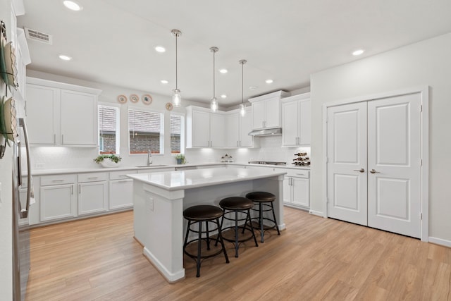 247 N Wild Petunia Trl, Montgomery, TX 77316 - kitchen featuring under cabinet range hood, gas cooktop, light wood finished floors, backsplash, and a kitchen island