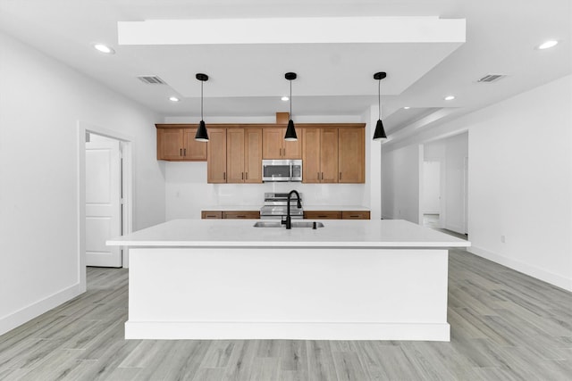 1005 Lake View Dr, Montgomery, TX 77356 - kitchen featuring stainless steel microwave, light countertops, brown cabinetry, a center island with sink, and light wood-type flooring