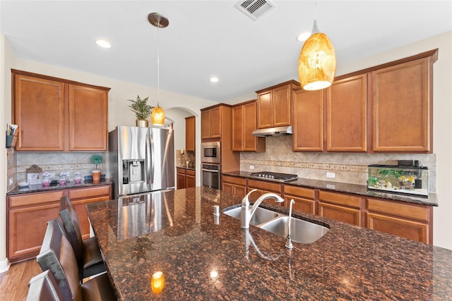 3614 Bonnie Bend Ln, Katy, TX 77494 - kitchen with stainless steel appliances, arched walkways, under cabinet range hood, brown cabinetry, and tasteful backsplash