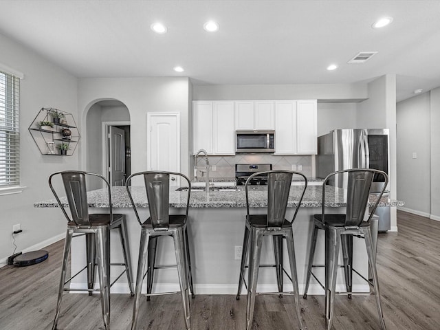 22010 Great Royal Ln, Houston, TX 77073 - kitchen featuring stainless steel appliances, a kitchen island with sink, light stone countertops, white cabinetry, and backsplash