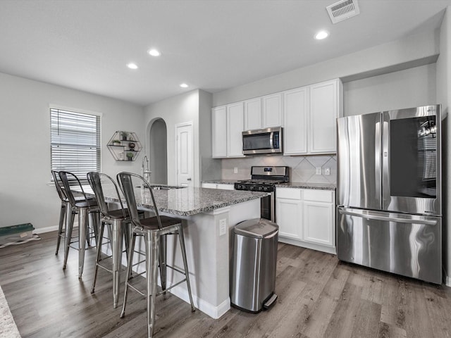 22010 Great Royal Ln, Houston, TX 77073 - kitchen with stainless steel appliances, wood finished floors, a center island with sink, stone counters, and arched walkways