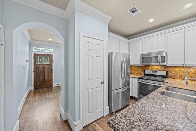 1773 Aden Dr, Houston, TX 77003 - kitchen with appliances with stainless steel finishes, crown molding, arched walkways, wood finished floors, and white cabinets