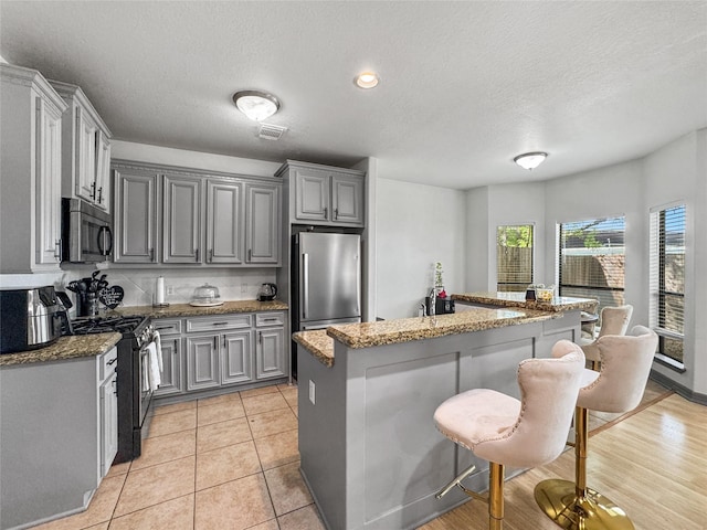 2905 Baer St Unit 6, Houston, TX 77020 - kitchen featuring stainless steel appliances, a breakfast bar, gray cabinets, a center island, and a textured ceiling