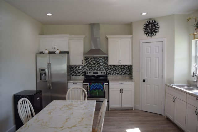 235 Rd 5253, Cleveland, TX 77327 - kitchen with wall chimney range hood, stainless steel appliances, light wood-style floors, white cabinetry, and backsplash