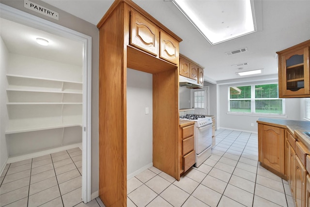 24193 Kelly St, Porter, TX 77365 - kitchen with white gas range, light tile patterned flooring, under cabinet range hood, glass insert cabinets, and brown cabinets