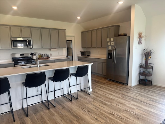 2944 Cordova Hill Dr, Katy, TX 77493 - kitchen with stainless steel appliances, gray cabinets, a breakfast bar, light wood-style flooring, and vaulted ceiling