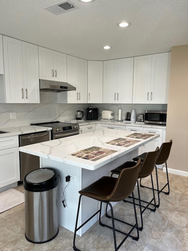 12117 Bob White Dr, Houston, TX 77035 - kitchen with appliances with stainless steel finishes, under cabinet range hood, a textured ceiling, a kitchen bar, and white cabinets