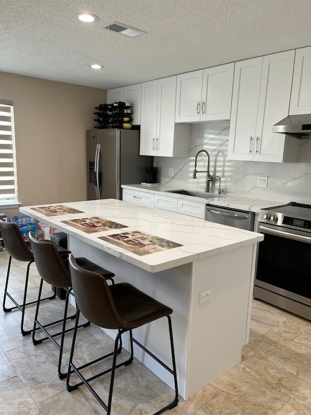12117 Bob White Dr, Houston, TX 77035 - kitchen with stainless steel appliances, under cabinet range hood, a kitchen bar, a center island, and white cabinets