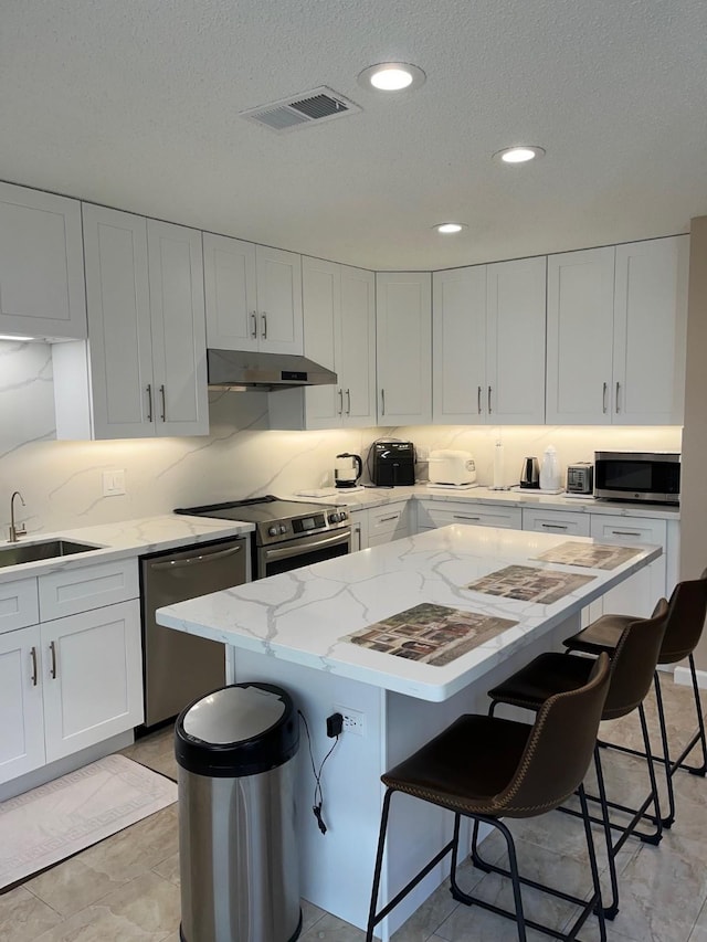 12117 Bob White Dr, Houston, TX 77035 - kitchen featuring stainless steel appliances, under cabinet range hood, a breakfast bar, white cabinets, and a center island