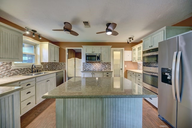 5425 Sandy Creek Ln, Brenham, TX 77833 - kitchen featuring stainless steel appliances, a ceiling fan, a kitchen island, wood finished floors, and backsplash
