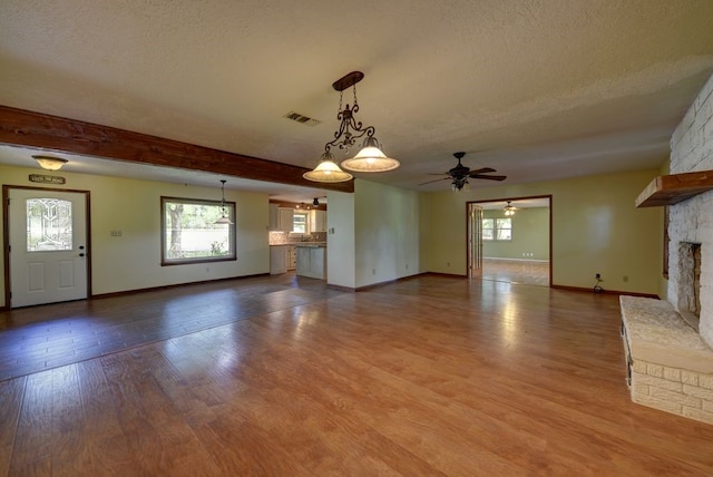 5425 Sandy Creek Ln, Brenham, TX 77833 - unfurnished living room with ceiling fan, a textured ceiling, a stone fireplace, and wood finished floors
