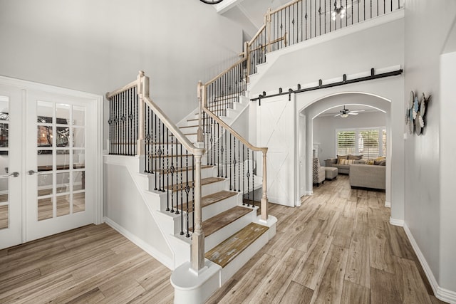 3506 Stanbury Place Ln, Katy, TX 77494 - staircase featuring a towering ceiling, a barn door, arched walkways, ceiling fan, and wood finished floors