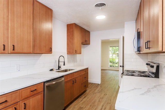 4640 Fieldwood Ln, Beaumont, TX 77706 - kitchen with appliances with stainless steel finishes, light wood-type flooring, light stone counters, decorative backsplash, and brown cabinets