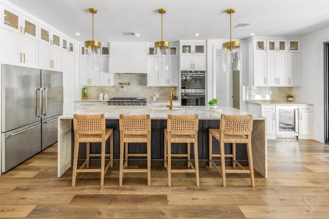 27706 Lakeway Trail Ln, Fulshear, TX 77441 - kitchen featuring appliances with stainless steel finishes, wine cooler, backsplash, wood finished floors, and a large island with sink