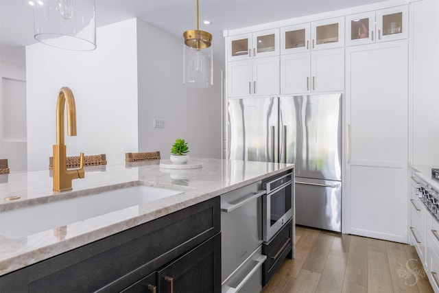 27706 Lakeway Trail Ln, Fulshear, TX 77441 - kitchen featuring appliances with stainless steel finishes, white cabinetry, light wood-type flooring, glass insert cabinets, and light stone countertops