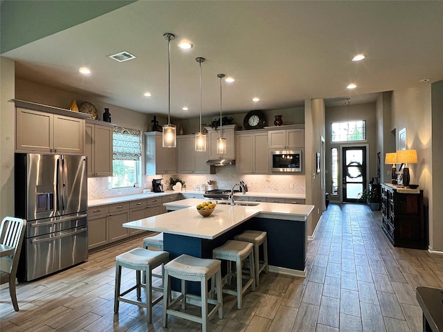 2 Ruchill Cir, Conroe, TX 77304 - kitchen with stainless steel appliances, light countertops, an island with sink, light wood-style flooring, and tasteful backsplash