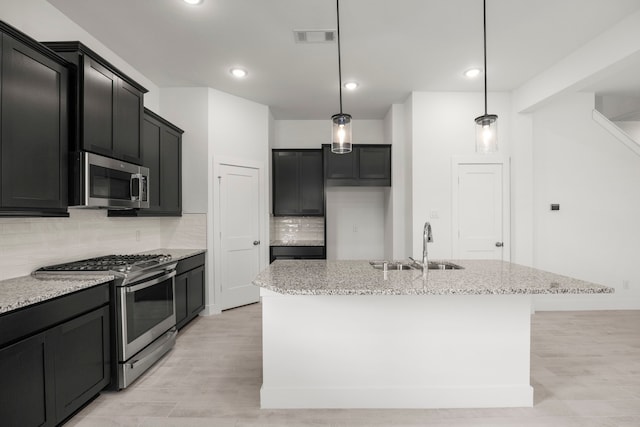 7810 Starfish Arbor Dr, Cypress, TX 77433 - kitchen with stainless steel appliances, light stone counters, tasteful backsplash, dark cabinetry, and a center island with sink