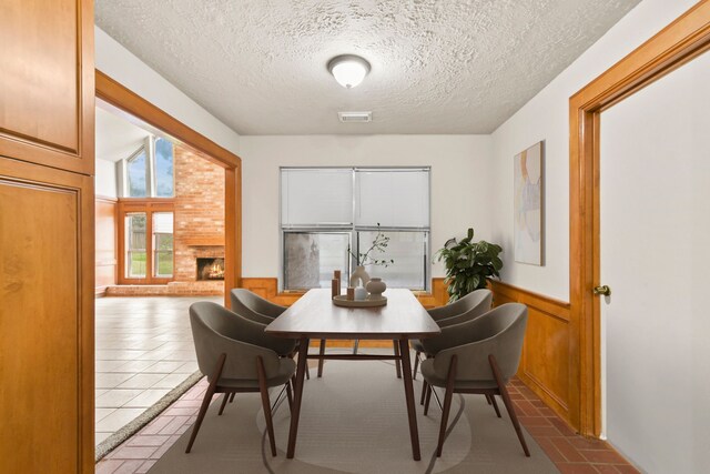 3735 Pineleaf Dr, Houston, TX 77068 - tiled dining room featuring a textured ceiling, wainscoting, and a fireplace