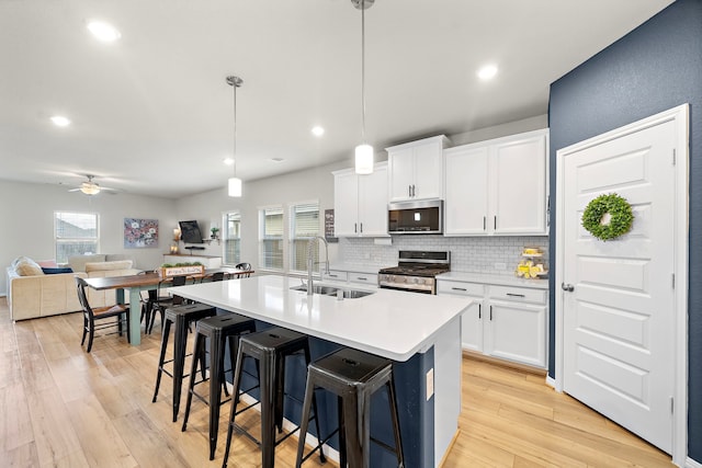 2218 Royal Ann Way, Tomball, TX 77375 - kitchen featuring appliances with stainless steel finishes, backsplash, ceiling fan, a center island with sink, and light wood-style floors