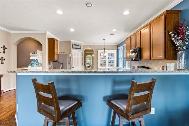 4472 Gerona St, League City, TX 77573 - kitchen featuring stainless steel fridge, black microwave, brown cabinets, arched walkways, and light stone countertops