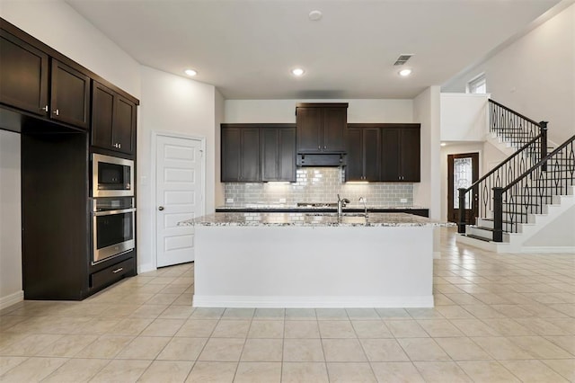 24239 Oakland Mist Ln, Katy, TX 77494 - kitchen featuring appliances with stainless steel finishes, backsplash, a center island with sink, light stone counters, and extractor fan