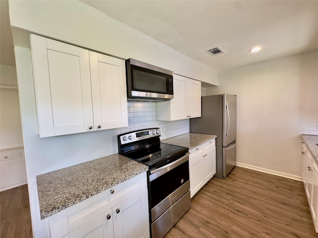 4310 Gallagher Dr, Houston, TX 77045 - kitchen featuring appliances with stainless steel finishes, wood finished floors, white cabinets, backsplash, and light stone countertops