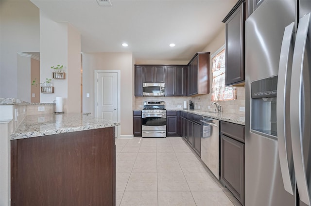 19547 Stetson Heights Ln, Richmond, TX 77407 - kitchen with stainless steel appliances, light tile patterned floors, dark brown cabinets, backsplash, and light stone counters