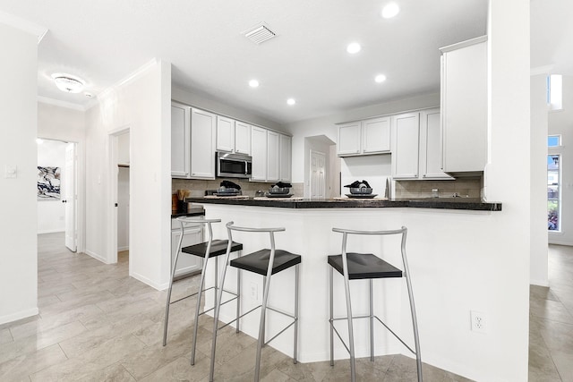23010 Adwick Ct, Katy, TX 77450 - kitchen with stainless steel microwave, a breakfast bar area, tasteful backsplash, crown molding, and recessed lighting