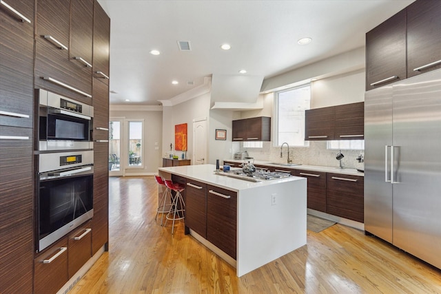 3926 Oberlin St, West University Place, TX 77005 - kitchen with stainless steel appliances, modern cabinets, ornamental molding, a kitchen bar, and light wood finished floors