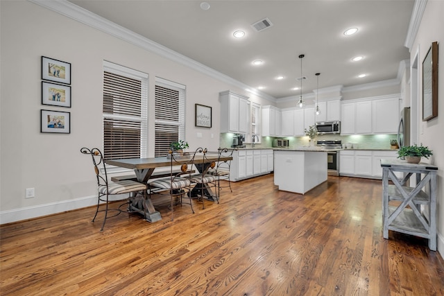 8720 Kempwood Dr, Houston, TX 77080 - kitchen with stainless steel appliances, crown molding, a kitchen island, wood finished floors, and white cabinetry