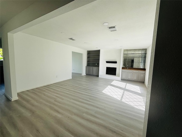 16246 Los Altos Dr, Houston, TX 77083 - unfurnished living room with built in shelves, light wood finished floors, a large fireplace, recessed lighting, and plenty of natural light