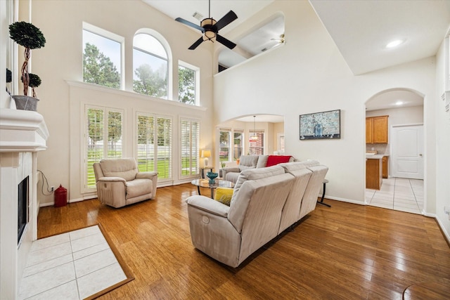 17326 Mesquite Brush Ln, Houston, TX 77095 - living area with arched walkways, ceiling fan, light wood-type flooring, a tiled fireplace, and a high ceiling