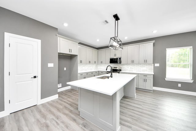 601 Lily St, Waller, TX 77484 - kitchen with appliances with stainless steel finishes, light countertops, backsplash, a kitchen island with sink, and light wood-style flooring