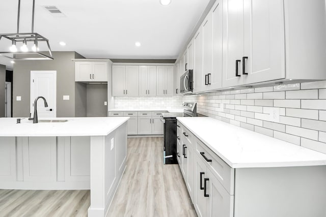 601 Lily St, Waller, TX 77484 - kitchen featuring appliances with stainless steel finishes, light wood-type flooring, backsplash, an island with sink, and decorative light fixtures