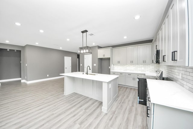 601 Lily St, Waller, TX 77484 - kitchen featuring stove, stainless steel microwave, tasteful backsplash, light wood-type flooring, and a kitchen island with sink