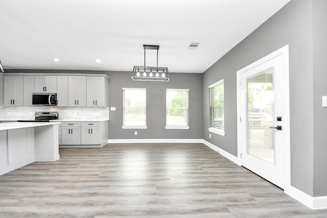 601 Lily St, Waller, TX 77484 - kitchen featuring appliances with stainless steel finishes, light countertops, tasteful backsplash, decorative light fixtures, and light wood-style flooring