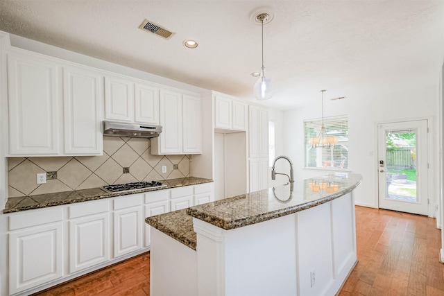 13811 Pepperstone Ln, Houston, TX 77044 - kitchen featuring under cabinet range hood, stainless steel gas cooktop, light wood-style floors, dark stone countertops, and tasteful backsplash