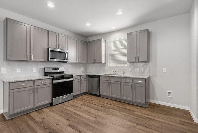 2580 Westslope Dr, Conroe, TX 77384 - kitchen with appliances with stainless steel finishes, gray cabinetry, wood finished floors, backsplash, and light stone countertops