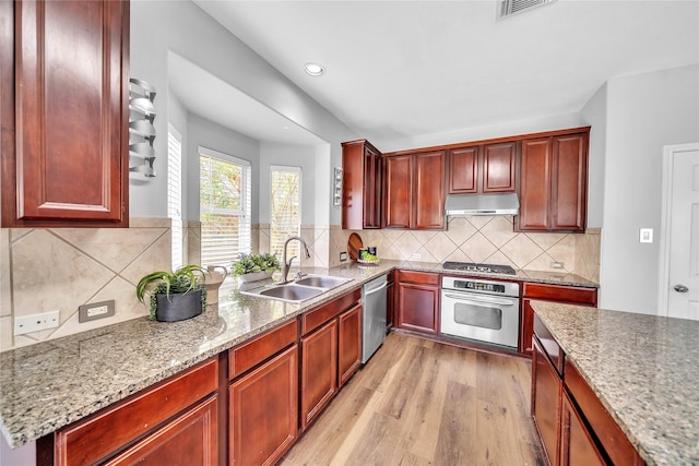 21142 Granite Trail Ln, Richmond, TX 77407 - kitchen featuring stainless steel appliances, under cabinet range hood, reddish brown cabinets, light wood-style flooring, and recessed lighting